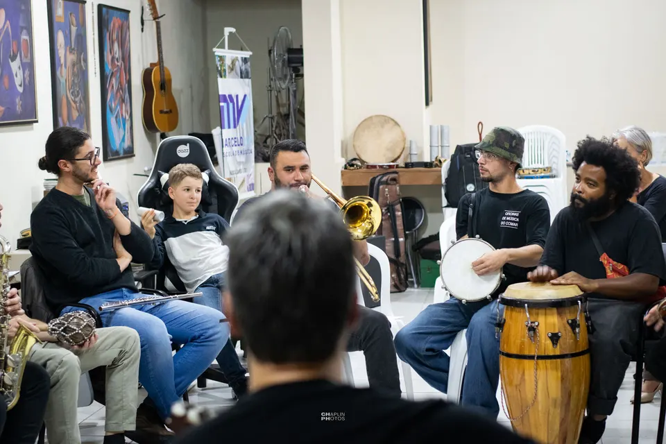 Roda de percussão com alunos e convidados, entre instrumentos e quadros coloridos.