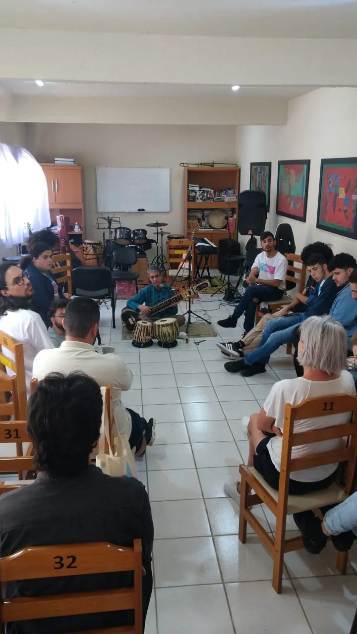 A sala Mentes MusiCaos cheia, com o público em cadeiras durante uma oficina.