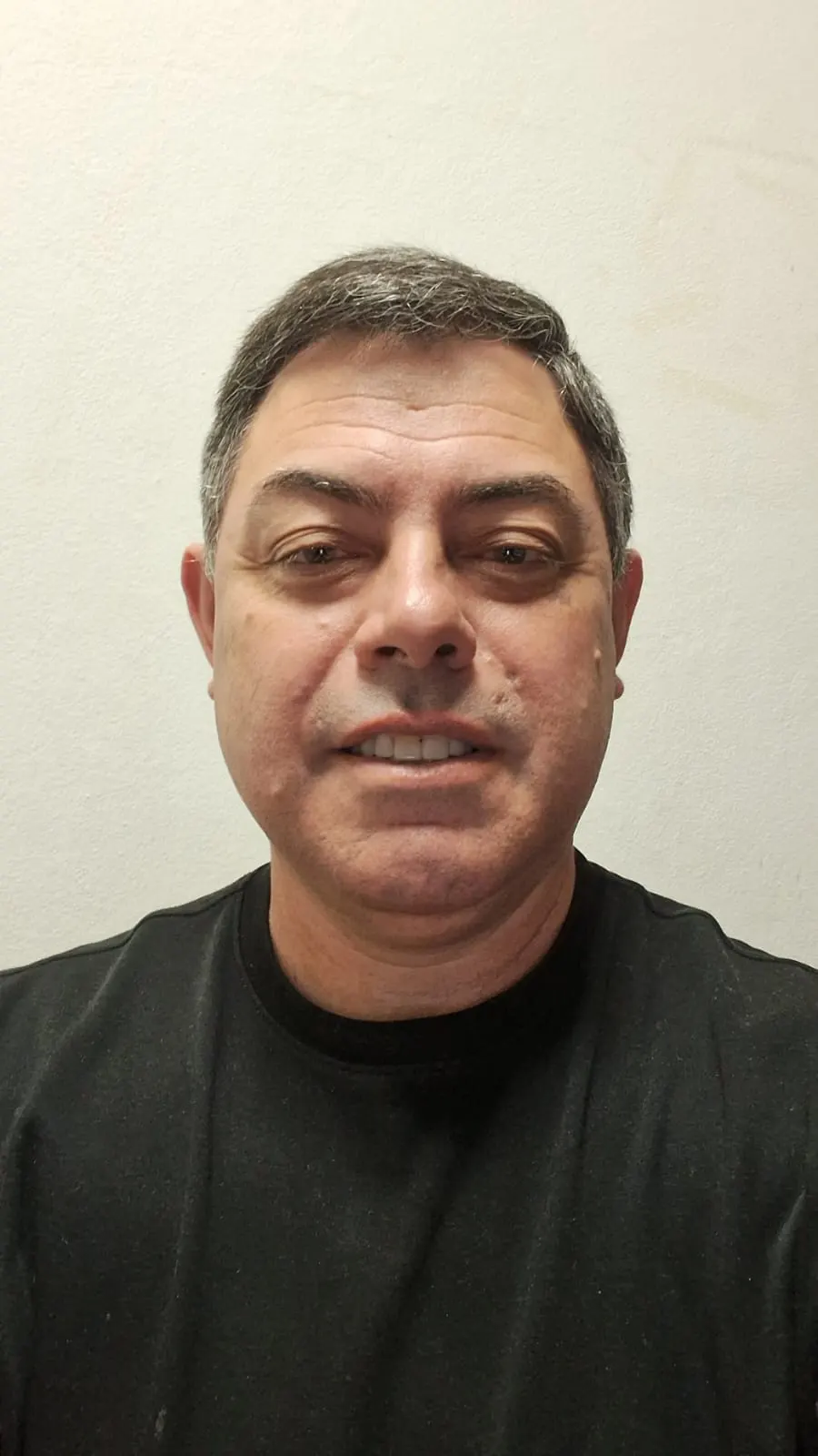 Alexandre Sales, de camiseta preta, diante de uma parede clara.