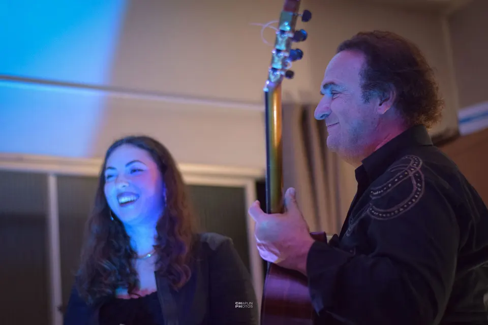 Cantora e violonista sorriem um para o outro durante uma apresentação de voz e violão.
