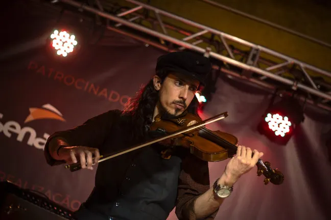 Dom Marquez toca violino num palco, de boina, sob luzes vermelhas.