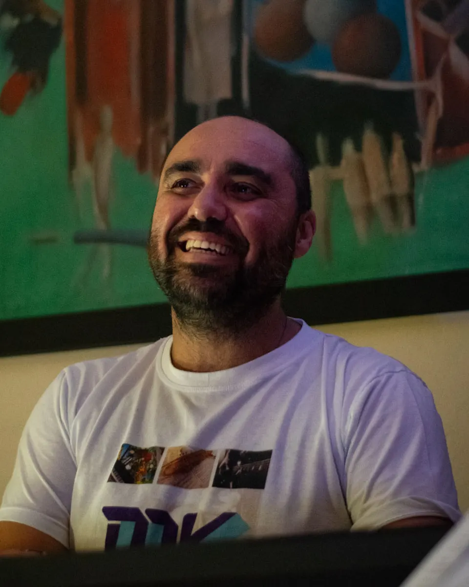 Marcelo Vaz sorri ao teclado, com um quadro colorido ao fundo.