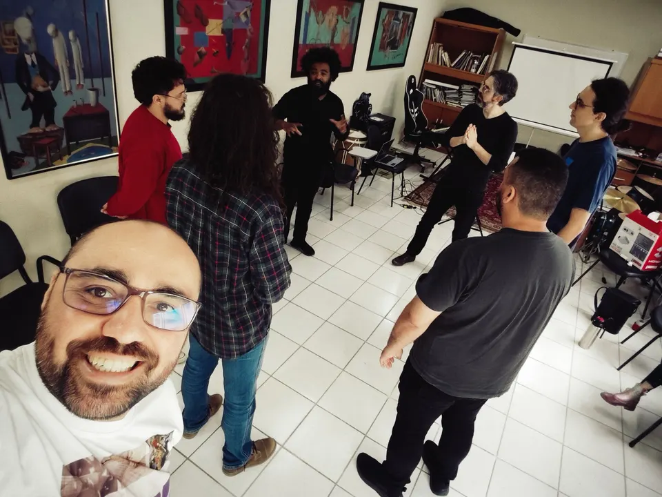 Selfie do Marcelo Vaz com os participantes de uma oficina do 2º Mentes MusiCaos, de pé na sala.